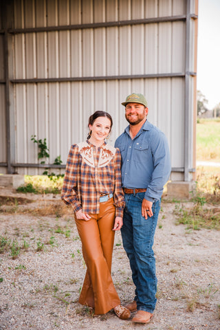 Model in the CORE Blue long sleeve pearl snap shirt with jeans and boots beside a woman in a plaid Western blouse.