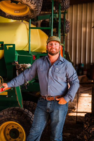 Front view of the CORE Blue long sleeve pearl snap shirt with two flap chest pockets, worn with jeans beside farm equipment.
