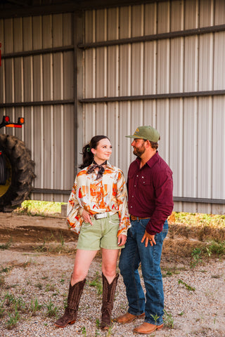 Model in the CORE Maroon long sleeve pearl snap shirt with jeans and boots beside a woman in a printed blouse and shorts.
