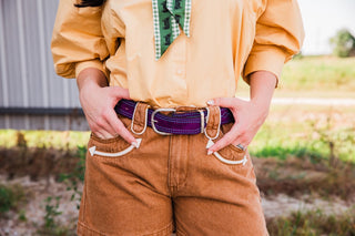 Front detail of the Double J Saddlery purple suede belt with turquoise stitching and a silver-tone buckle, worn with tan shorts.