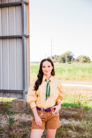 Model wearing the Double J Saddlery purple suede belt with turquoise stitching, tan Western shorts, and a tucked-in blouse.