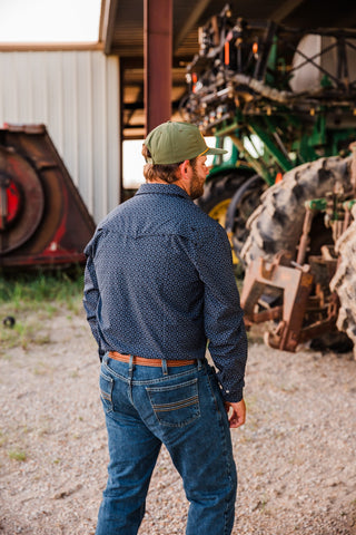 Back view of the Ferrell Silas black long sleeve pearl snap shirt, showing its geometric print and back yoke with jeans.