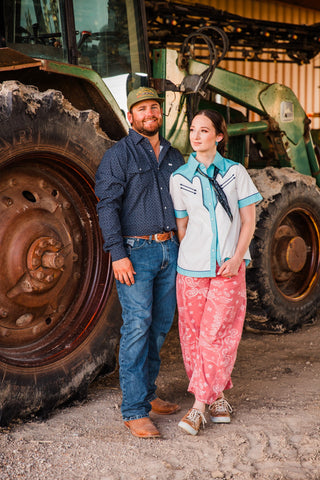 Man wearing the Ferrell Silas black long sleeve pearl snap with jeans and brown boots, standing beside a woman at a tractor.