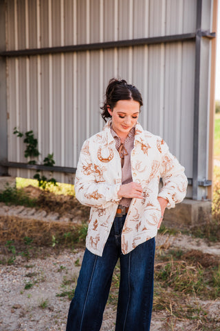 Model wearing the cream and brown Frontier Jacket with a gingham blouse, tan belt and dark wash wide-leg jeans outdoors.