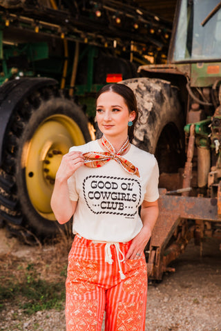 Good Ol’ Cowgirls Club cream graphic tee worn with an orange neck scarf and drawstring pants, showing its short sleeves.