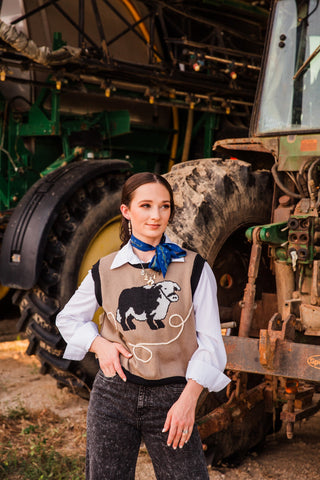 Model wearing the Hold Your Horses Navy Twilly above a white collar and tan cattle vest, posing beside a tractor.