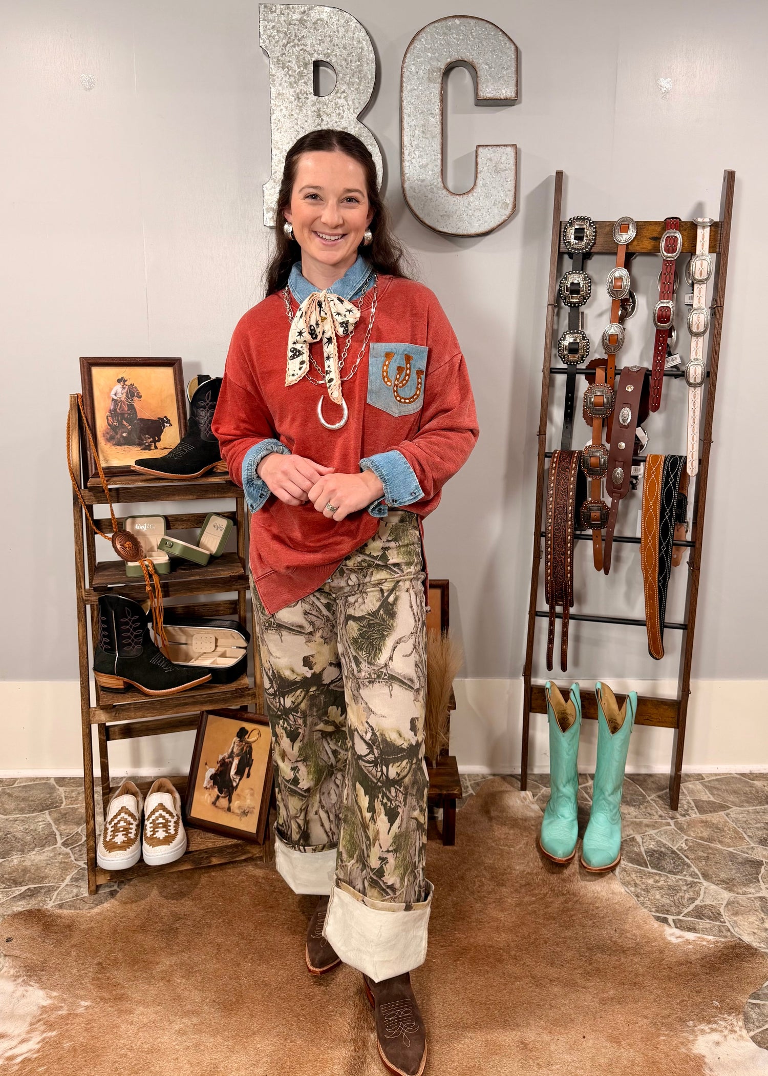 Person wearing a red shirt and camouflage pants standing in a store with cowboy boots and belts displayed.