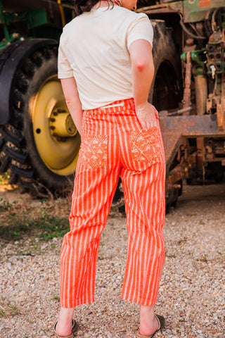Back view of Everyday Outlaw Pants by Howdy Hanny with red-orange vertical stripes, patterned patch pockets and ankle-length hems.