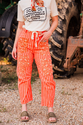 Everyday Outlaw striped pants with patterned front pockets and knee panels, styled with a cream graphic tee and slide sandals.