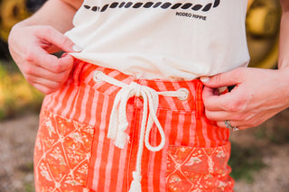 Close-up of Everyday Outlaw Pants showing a cream rope drawstring through metal eyelets, striped waistband and patterned pockets.