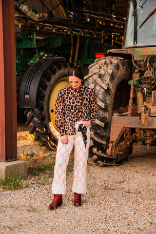 Full-length view of the Penny leopard blouse worn partly tucked into cream patterned pants with wide cuffs and red boots.