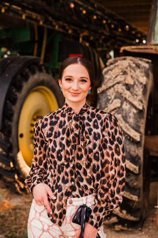 Front view of the Howdy Hanny Penny leopard blouse with a tied neckline, button front, puff shoulders and long cuffed sleeves.