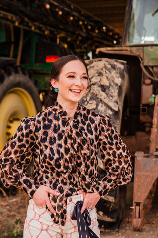 Penny leopard print blouse on a smiling model with hands at her waist, showing puff sleeves, fitted cuffs and a matching neck tie.