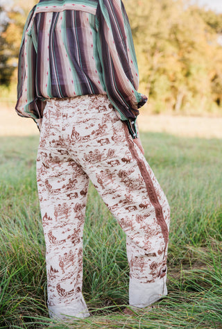 Rear angled view of Howdy Hanny Ranch Life Barrel Jeans with brown ranch print, back pockets, side trim and rolled cuffs.