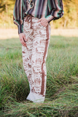 Side detail of Howdy Hanny Ranch Life Barrel Jeans showing brown Western scenes, patterned side trim and a rolled cream cuff.