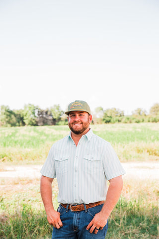 Jack in Green striped short sleeve pearl snap shirt styled with blue jeans and a tooled brown belt in an outdoor setting.