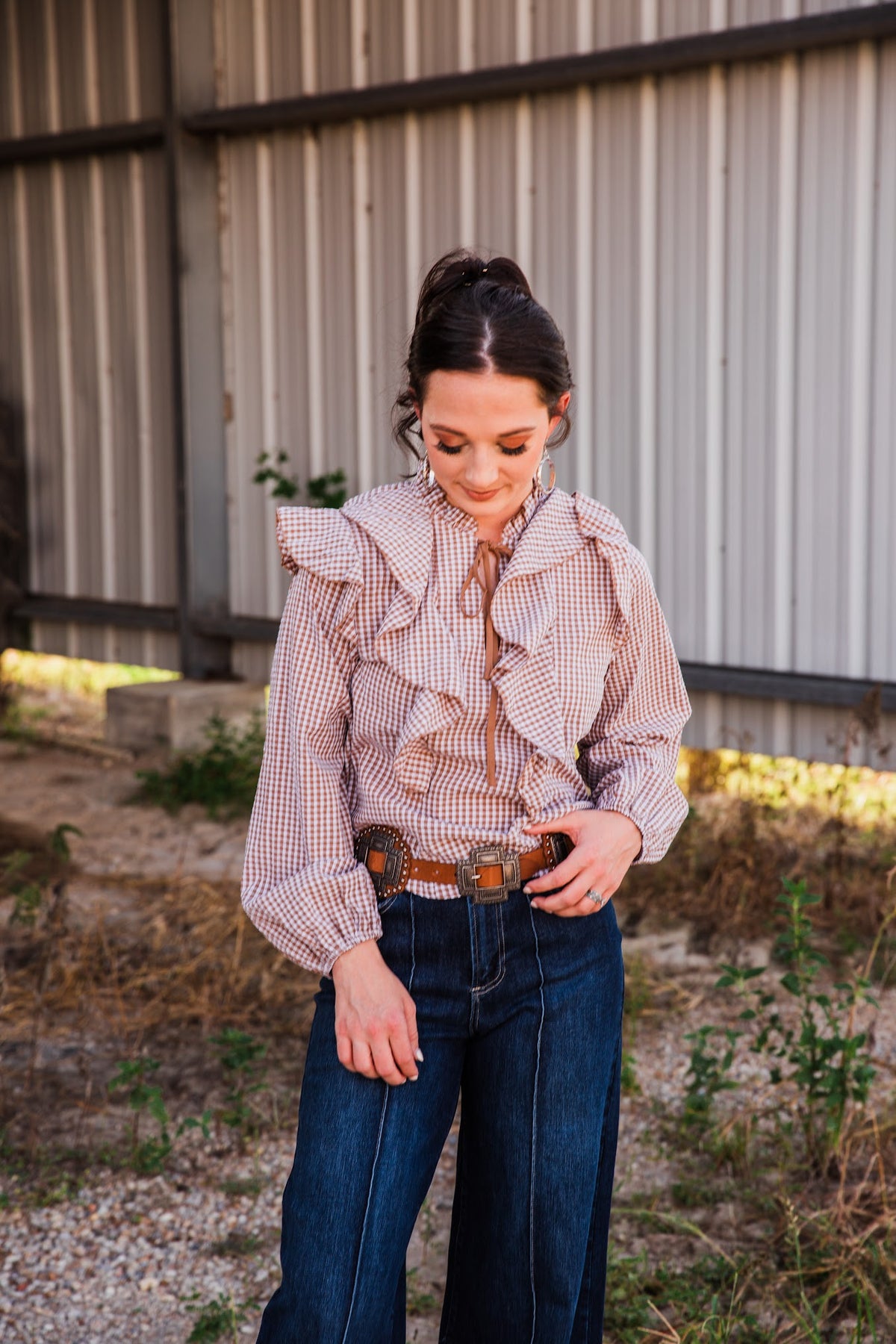 Jincy Top brown gingham ruffle blouse showing its full long sleeves and gathered cuffs, tucked into dark denim jeans.