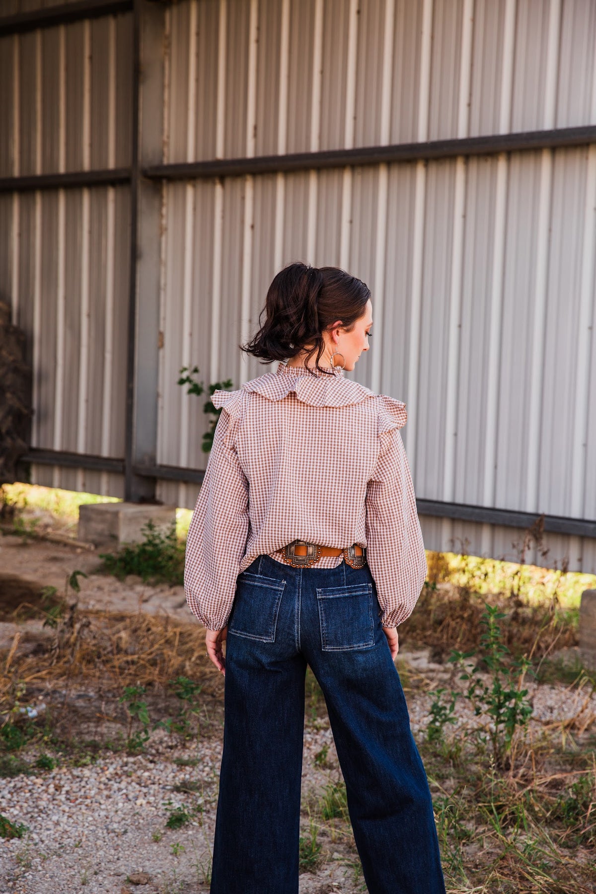 Back view of the Jincy Top brown gingham blouse, showing its ruffled collar, shoulder ruffles and long gathered sleeves.