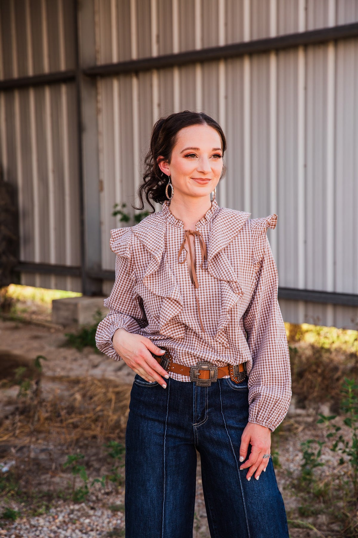 Front view of the Jincy Top brown gingham blouse with shoulder and chest ruffles, a tie neckline and gathered cuffs.
