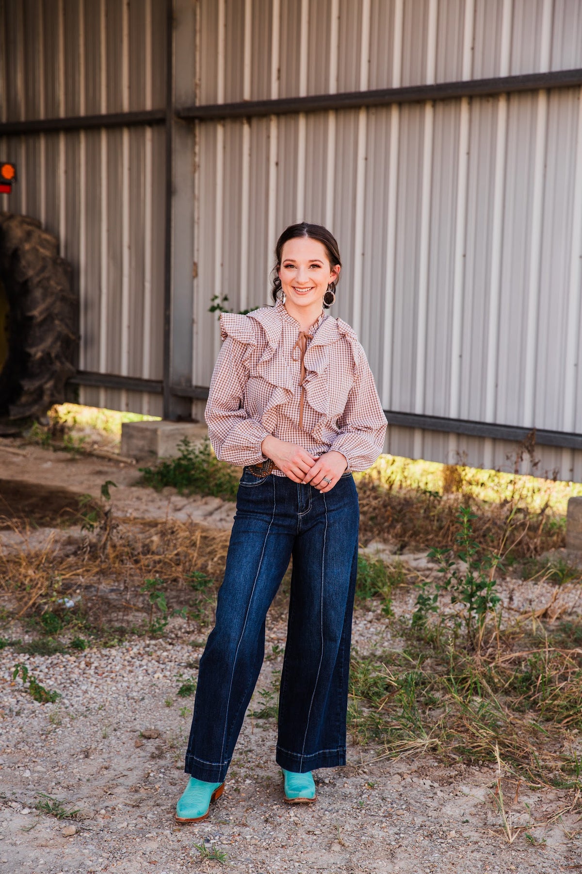 Full outfit view of a model wearing the Jincy Top gingham ruffle blouse with wide-leg jeans and turquoise boots outdoors.