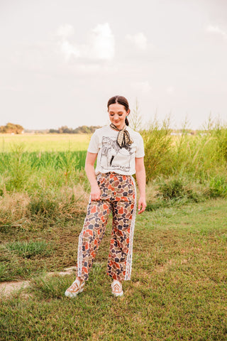 Keepin’ It Western cream graphic tee tucked into multicolor patterned pants with lace side trim, paired with tan sneakers.