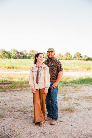 Lee caramel faux leather wide-leg pants styled with an embroidered cream blouse in an outdoor couple portrait.