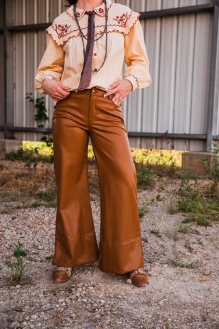 Lee caramel brown mid-rise faux leather pants with the waistband visible, showing a button closure and wide-leg silhouette.