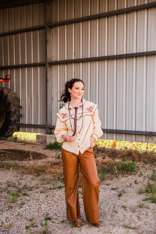 Full-length look at Lee caramel brown mid-rise wide-leg faux leather pants paired with a cream blouse and layered necklaces.