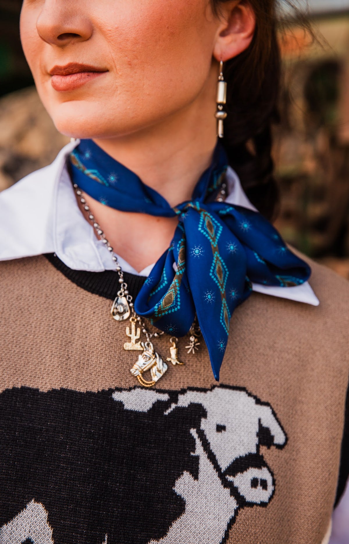 Legacy Bloom silver drop earring styled with a blue patterned neck scarf, white collared shirt and tan cow-print sweater vest.