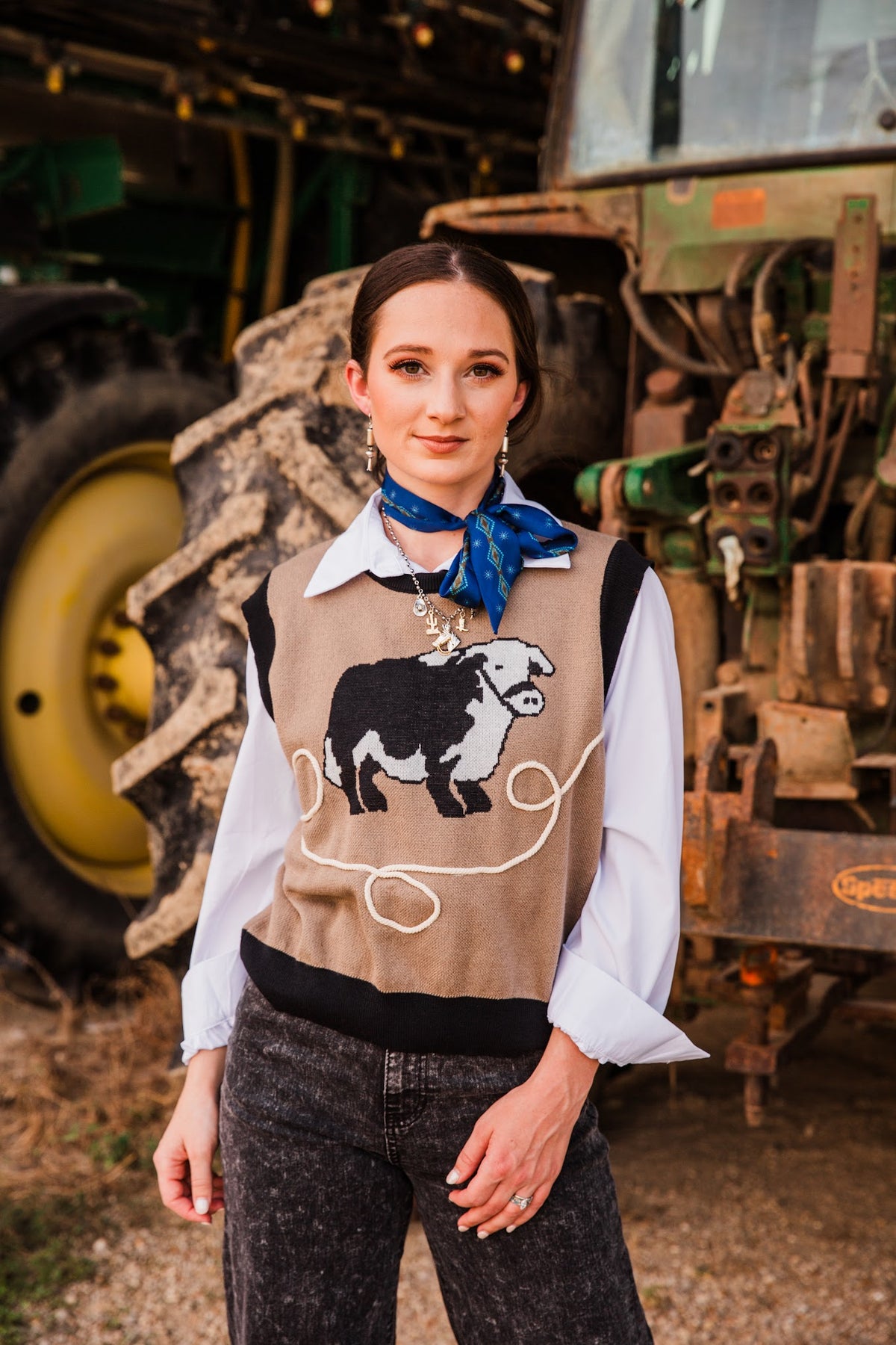 Model wearing Legacy Bloom sterling silver earrings with a blue neck scarf, tan cattle sweater vest and washed black jeans.