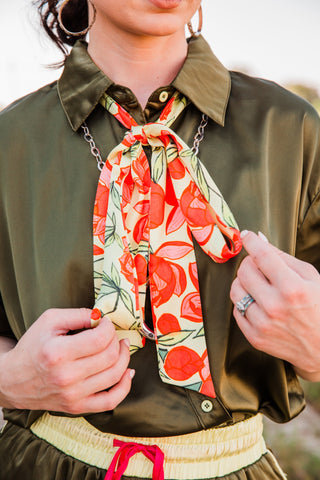 Close-up of the Lemon Bloom Satin Tie held open to show its coral citrus and green leaf print against an olive satin shirt.