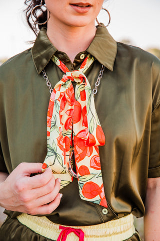 Lemon Bloom Satin Tie knotted beneath an olive shirt collar, with long pale yellow ends displaying coral citrus and green leaves.