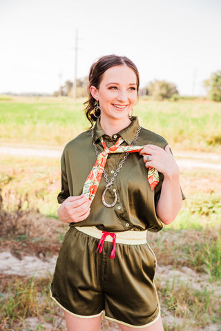 Model holding the ends of the Lemon Bloom Satin Tie, styled with an olive satin set and a silver-tone horseshoe necklace.