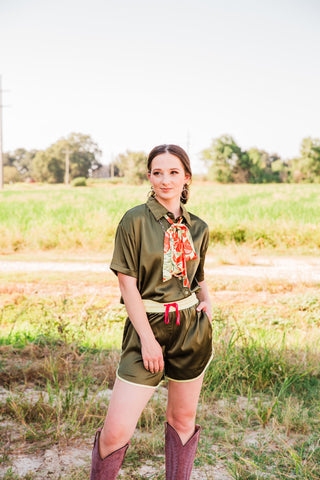 Lemon Bloom Satin Tie styled as a neck scarf with an olive satin shirt and shorts set and tall Western boots outdoors.