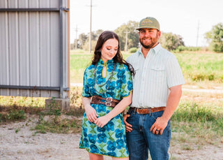 Sadie in the floral Lissie Mini Dress, size S/M, with a brown belt and turquoise boots, standing beside a man outdoors.