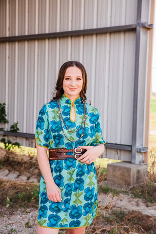 Sadie in size S/M of the Lissie Mini Dress, showing its yellow-trimmed keyhole neckline, blue flowers, and green leaves.
