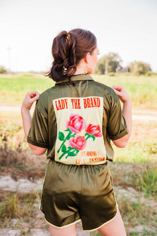Back view of Sadie in the Live Satin Set, size S/M, showing a cream rose graphic panel on the olive shirt and matching shorts.