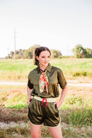 Sadie wears the olive green Live Satin Set in size S/M, featuring a collared shirt and matching shorts with cream trim.