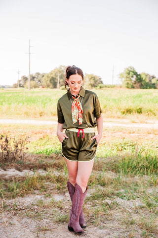 Full-length view of Sadie in the Live Satin Set, size S/M, with hands in the shorts pockets and the olive shirt tucked in.