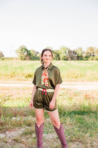 Sadie styles the olive green Live Satin Set in size S/M with a floral neck scarf and tall burgundy cowboy boots outdoors.