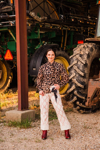 Sadie wears Lucky Babe Pants in Extra Small, styled with a leopard blouse and red boots, showing cream fabric and a red pattern.