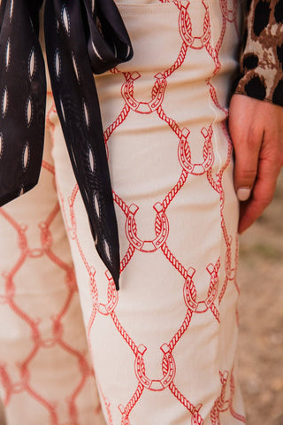 Close-up of Lucky Babe Pants showing red horseshoes linked by rope motifs on cream fabric, worn by Sadie in Extra Small.