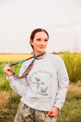 Model wearing the Nashville Twilly by Fringed Scarves, holding its turquoise and red geometric ends beside a gray sweatshirt.
