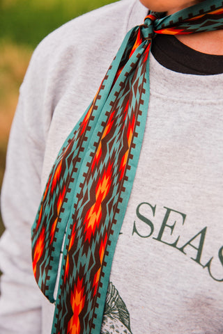 Close-up of Nashville Twilly by Fringed Scarves with turquoise, brown, red and gold Southwestern geometric print tied at the neck.