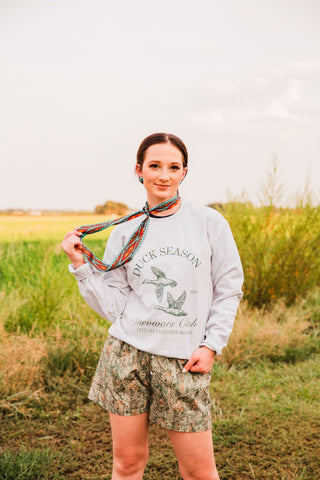 Nashville Southwestern print twilly styled as a neck scarf with a gray duck graphic sweatshirt and woodland camo shorts outdoors.