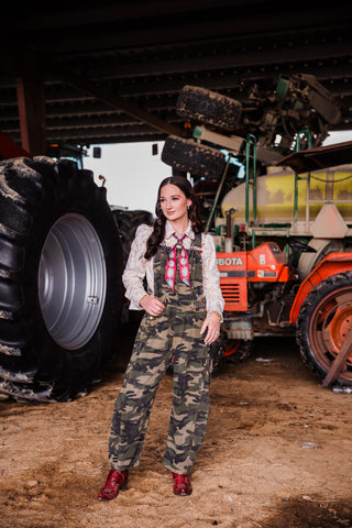 Women’s Western camouflage overalls layered over printed pearl snap shirt with red cowboy boots
