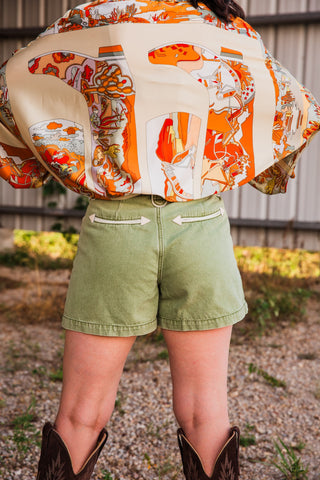Back view of Polly Olive denim shorts, showing cream arrow-tipped pocket trim, a center seam and stitched hems.