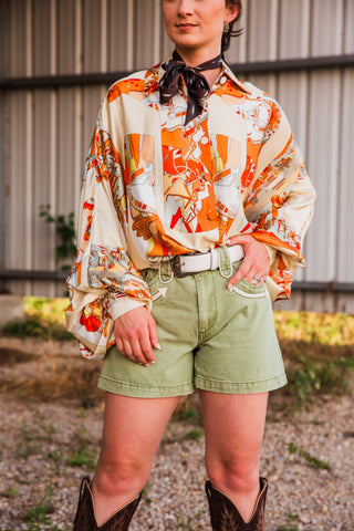 Polly Olive denim shorts on a model with one hand in a front pocket, showing cream contrast trim and neat stitched hems.