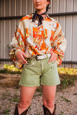 Front view of Polly Olive Shorts by Howdy Hanny, showing curved cream-trimmed pockets and wide belt loops with a white belt.