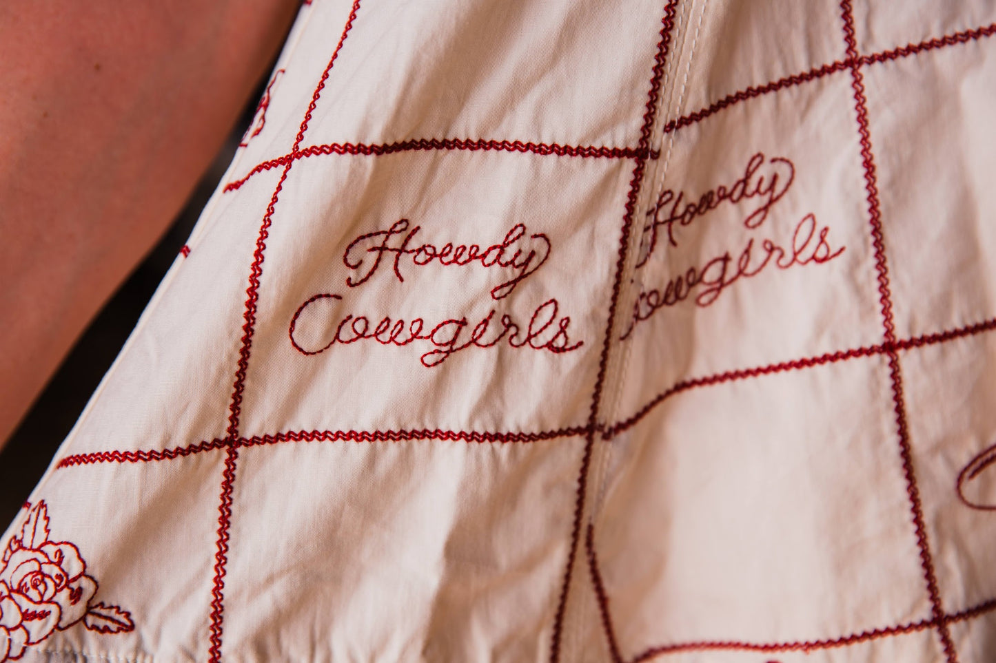 Close-up of a cream-colored quilted textile with red stitched grid lines and embroidered script reading 'Howdy Cowgirls'